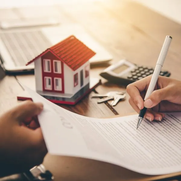 Persona che firma un contratto di ristrutturazione per il proprio appartamento con modello di abitazione sullo sfondo
