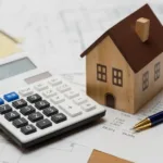 Modello di casa in legno sopra una calcolatrice e documenti finanziari