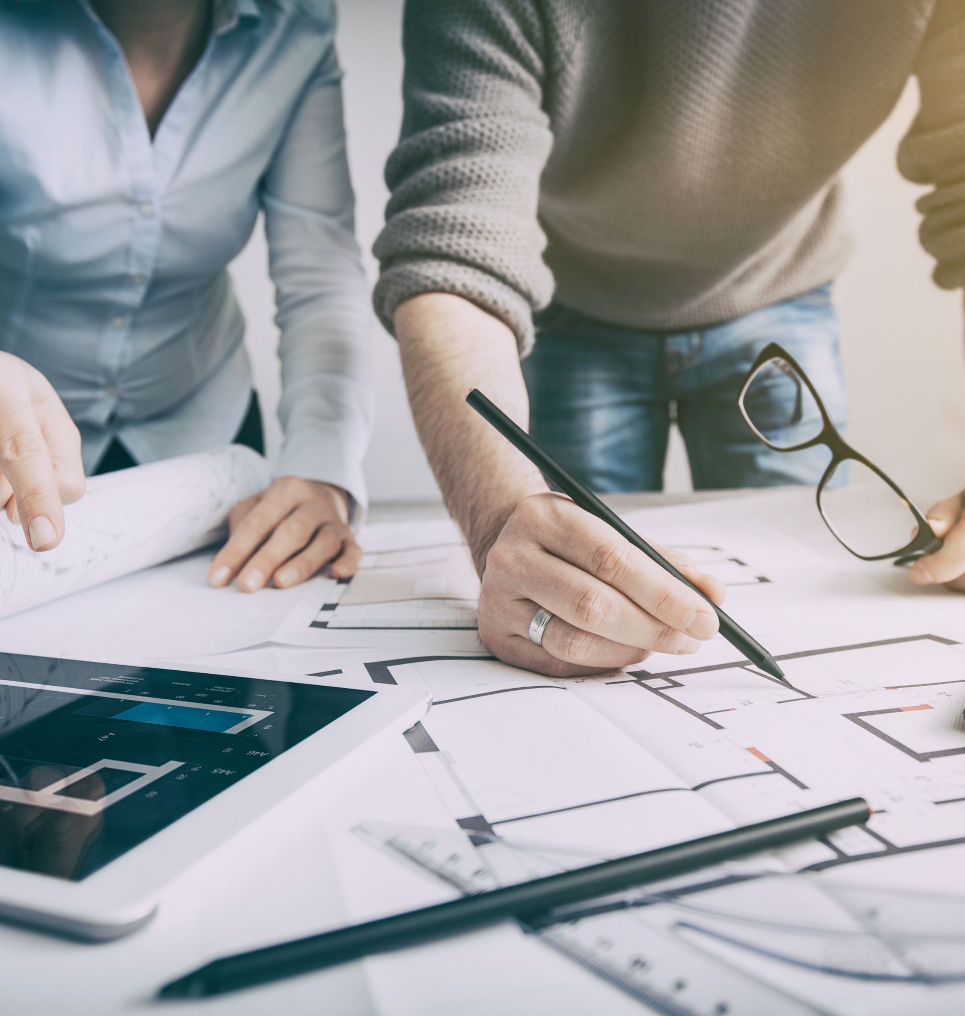 Duo di architetti lavora su planimetrie con dispositivi digitali e strumenti di progettazione su un tavolo