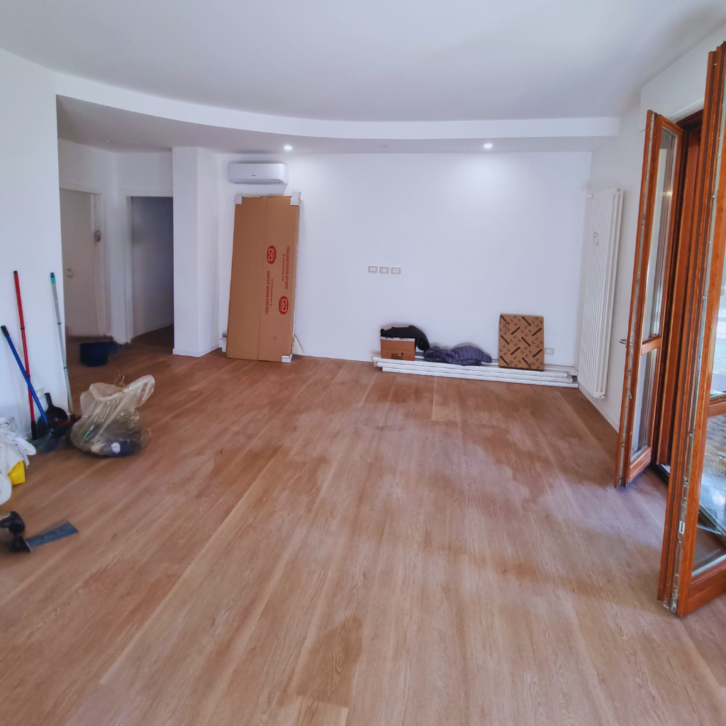 Soggiorno-salotto dopo la ristrutturazione, ambiente aperto integrato con ingresso, pareti bianche, pavimento effetto legno continuo e cartongesso a soffitto perimetrale — appartamento 100 mq Milano Garibaldi