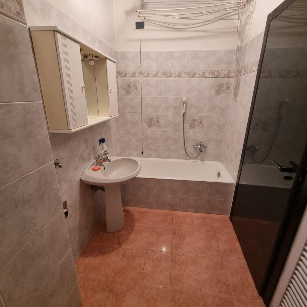 Bagno vasca prima (rivestimenti grigi con fascia decorativa, sanitari obsoleti, lavabo a colonna)