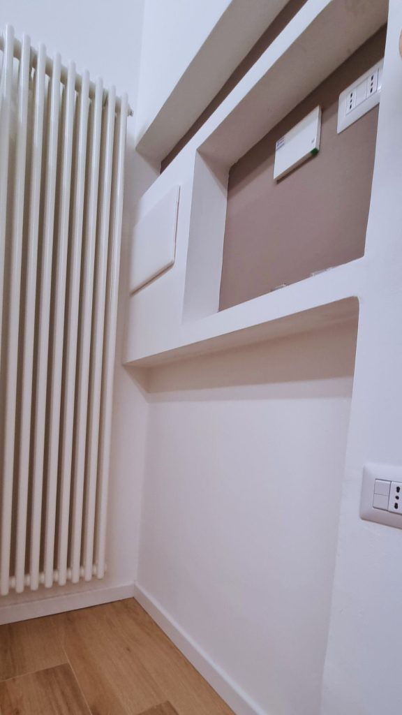 Dettaglio del termoarredo verticale accanto alla parete attrezzata con nicchie su misura, pensate per integrare quadri elettrici e dispositivi domotici in modo discreto ed estetico.