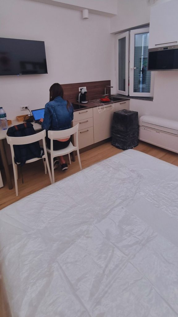 Vista d'insieme dell'angolo cucina e zona giorno del monolocale da 20 mq, con piano a induzione, mini tavolo da pranzo e letto matrimoniale integrati in un unico ambiente funzionale progettato per affitto breve.