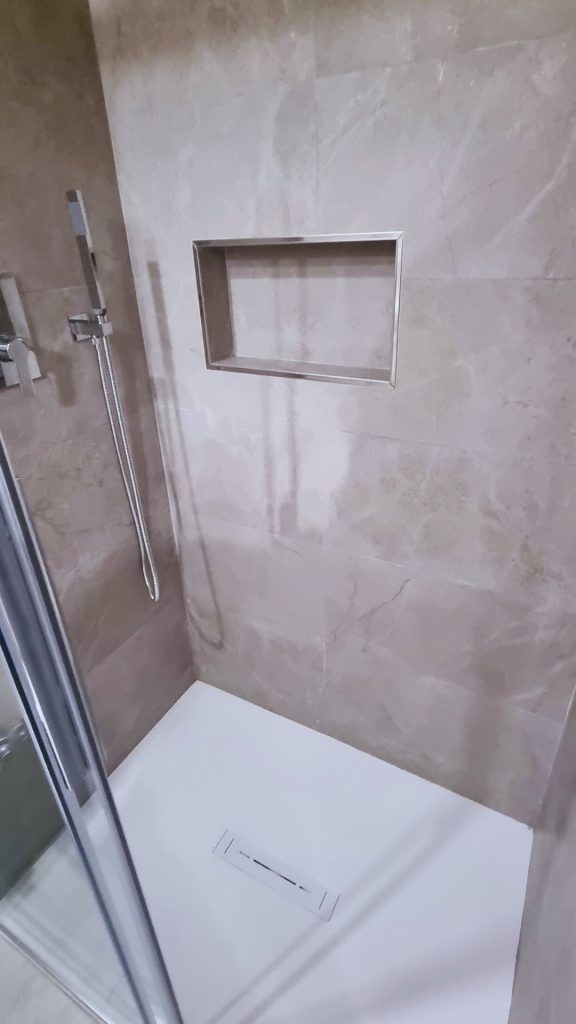 Dettaglio della doccia in nicchia realizzata su misura, con piatto filo pavimento e rivestimento in gres effetto marmo, completa di nicchia incassata per saponi e accessori.