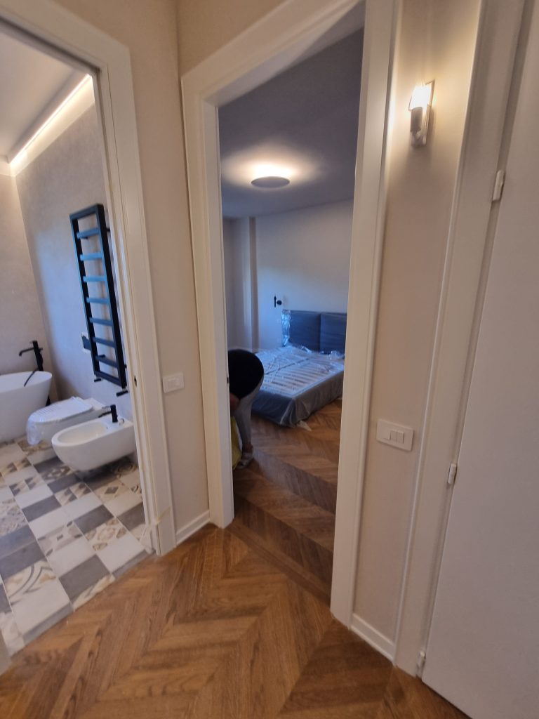 Corridoio con pavimento in parquet a spina di pesce, vista sul bagno e sulla camera da letto dopo la ristrutturazione dell'appartamento a Milano Cenisio.