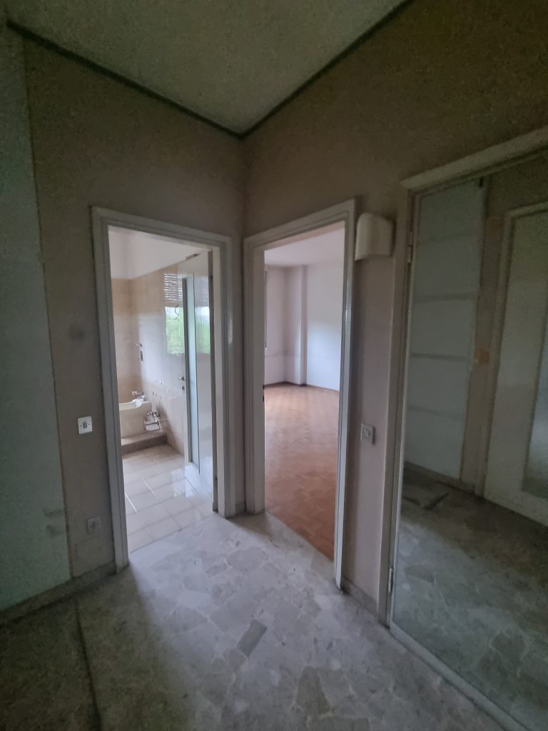 Corridoio con pavimento in marmo e porte vecchie, vista sul bagno e su una camera, prima della ristrutturazione dell'appartamento a Milano Cenisio.