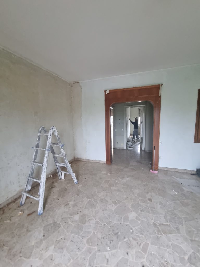 Soggiorno con pavimento in marmo vecchio, pareti in disordine e controsoffitto datato, prima della ristrutturazione dell'appartamento a Milano Cenisio.