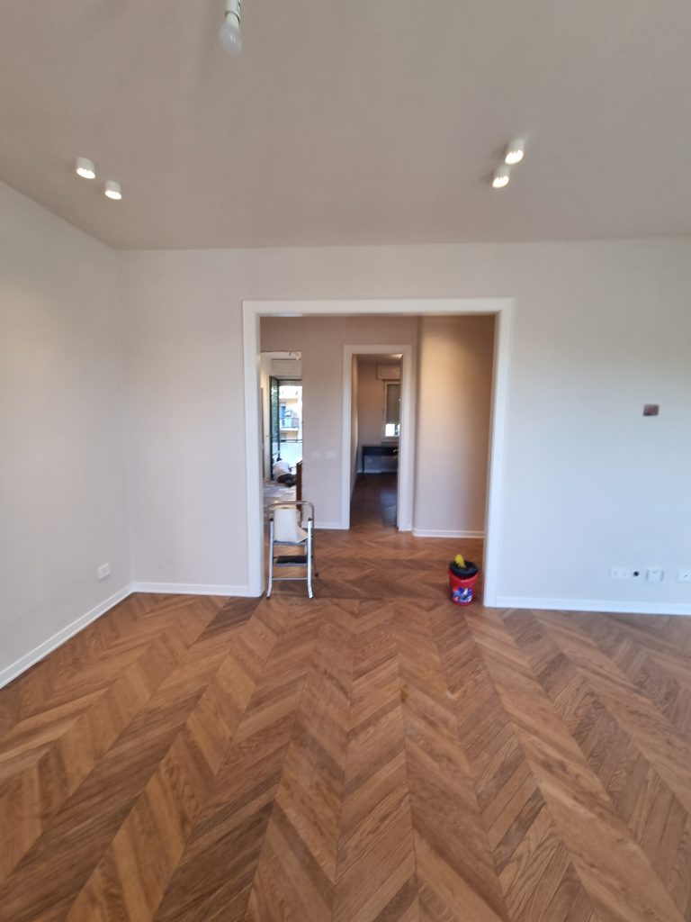 Nuovo soggiorno open space con pavimento in parquet a spina di pesce, pareti tinteggiate e illuminazione moderna, dopo la ristrutturazione dell'appartamento a Milano Cenisio.