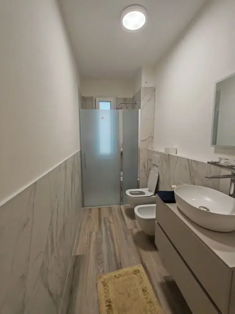 Bagno principale dopo – gres effetto marmo, sanitari sospesi e doccia vetro, ristrutturazione 115 mq Niguarda