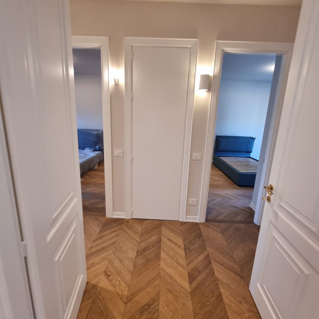 Corridoio con porte interne Garofoli, nuovo parquet e illuminazione moderna, dopo la ristrutturazione dell'appartamento a Milano Cenisio.