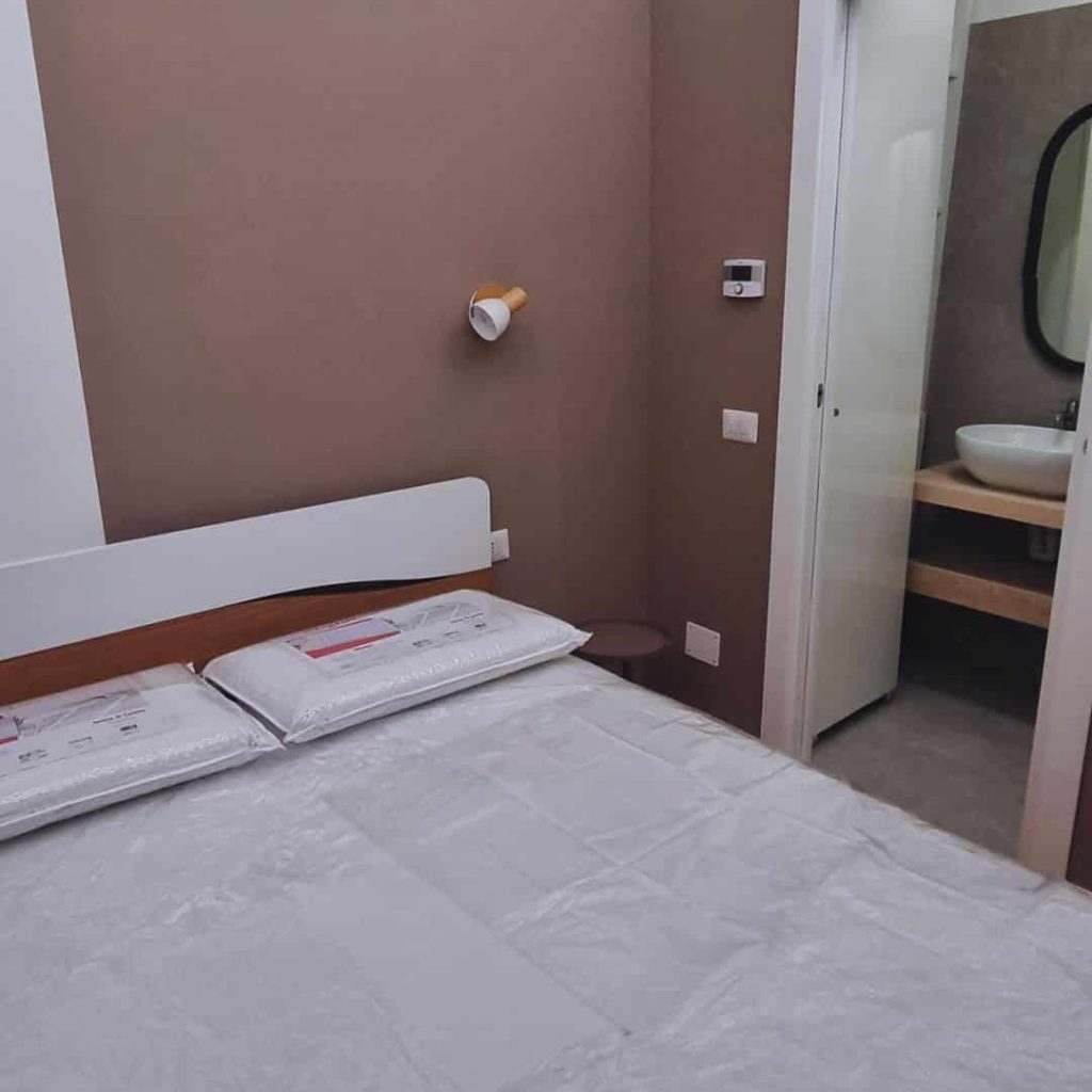Monolocale 20 mq Milano Isola dopo ristrutturazione, arredamento zona notte con letto matrimoniale e accesso diretto al bagno.
